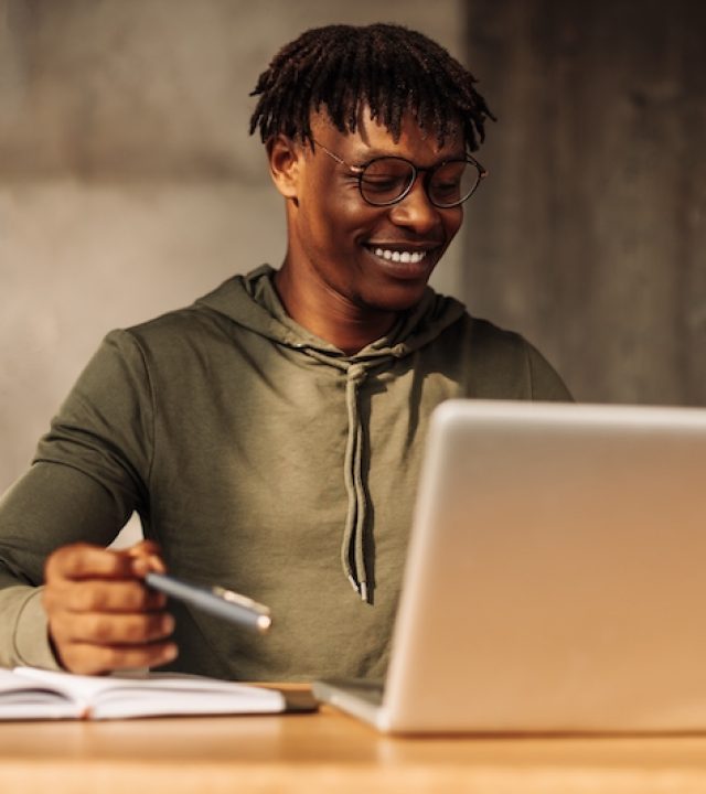 African American man with laptop and notepad at the table. a man writes with a pen in a notebook. distance learning. coaching, seminar, session, online conference. houses on isolation